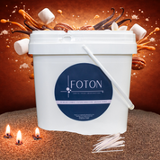 Large white Foton Pearled Candle bucket (XL-Kit) with handle shown against a caramel dessert-inspired background with caramel cubes, vanilla, pecans, and marshmallows, with small candle flames and cotton wicks in the foreground.
