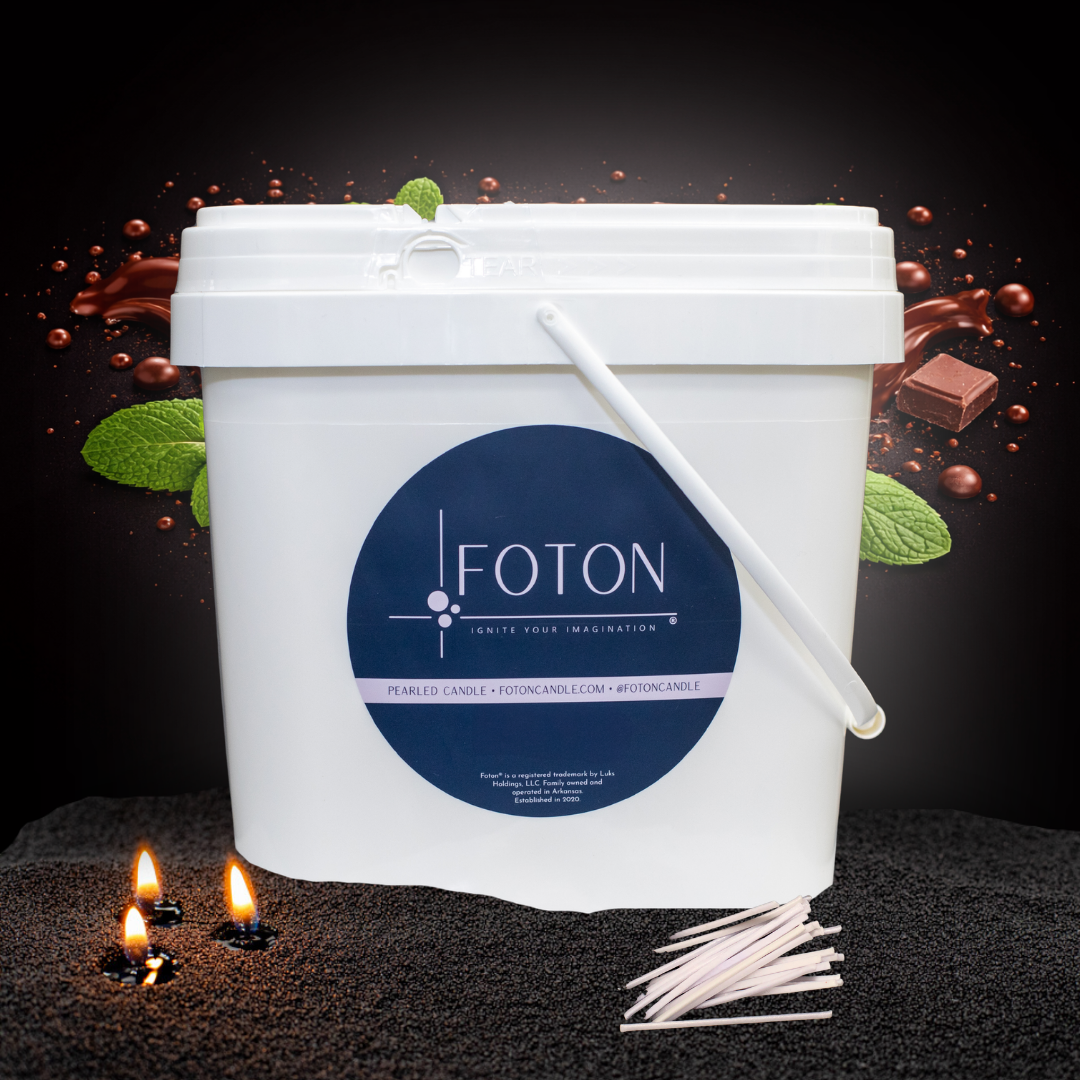 Large white Foton Pearled Candle bucket (XL-Kit) displayed against a dark chocolate and mint background with flowing chocolate and mint leaves, with cotton wicks and glowing candle flames in black wax pearls in the foreground.