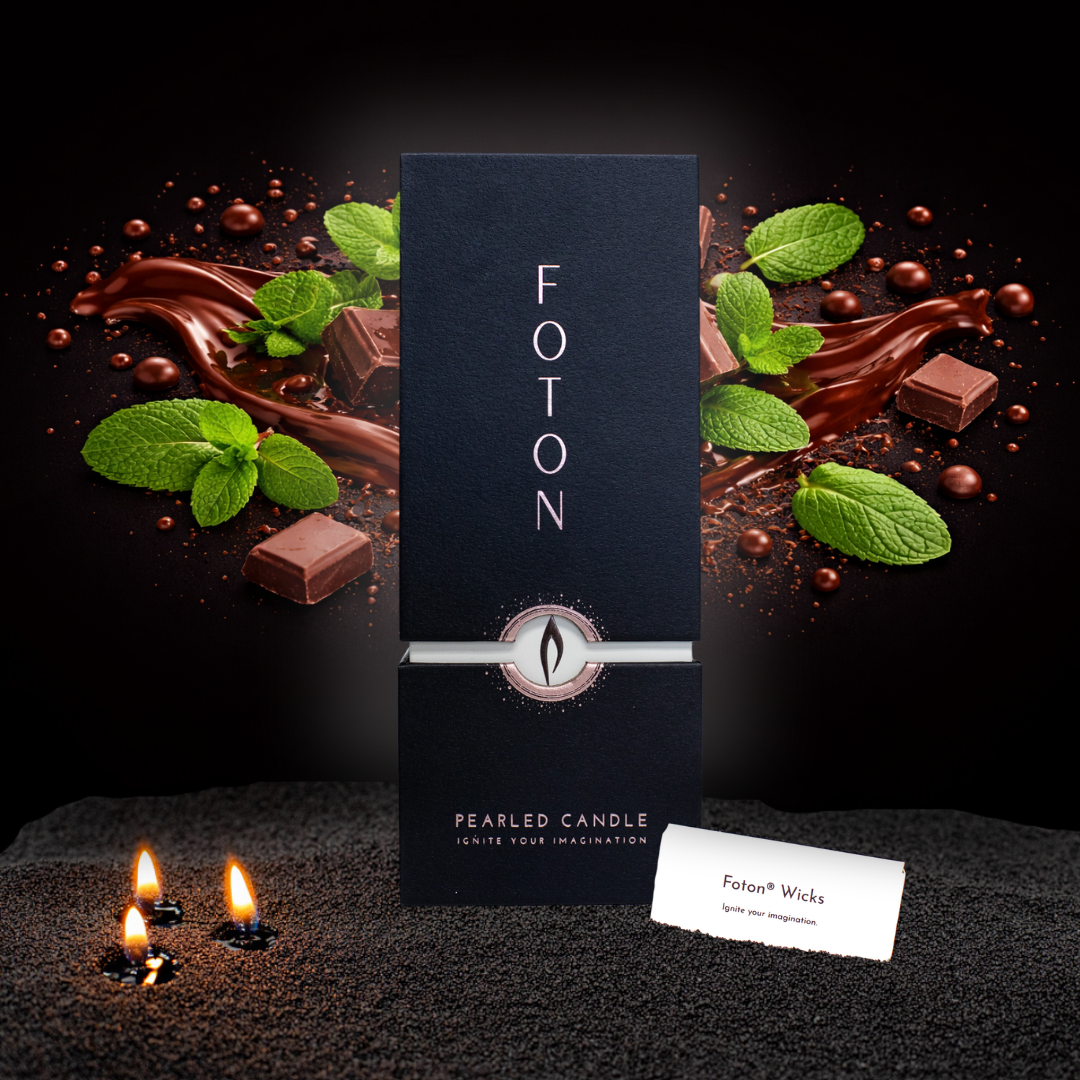 Black Foton Pearled Candle 18oz box against a dark background with flowing chocolate, chocolate pieces, and fresh mint leaves, with three small candle flames glowing in black wax pearls in the foreground.