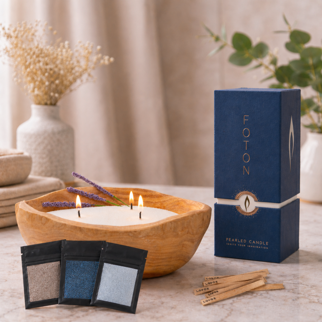 Styled product scene featuring a lit candle in a handcrafted wooden bowl with three flames and lavender accents. Nearby are three sample packs, wooden wicks, and a blue Foton Pearled Candle 18oz box, arranged on a neutral surface with soft lighting and natural decor in the background.