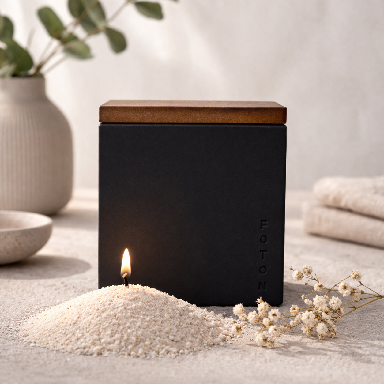 Lifestyle product image of the Le Cube candle in a matte black vessel, styled with soft florals and neutral textures to create a refined, modern, and calming ambiance.
