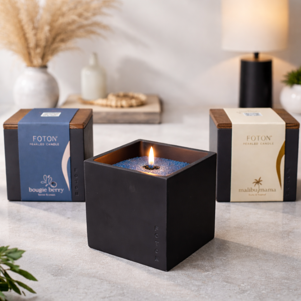 Lifestyle product image featuring the black Le Cube candle lit at center, styled with Bougie Berry and Malibu Mama packaging in the background, creating a refined, modern setting that highlights scent variety and elevates the overall brand presentation.