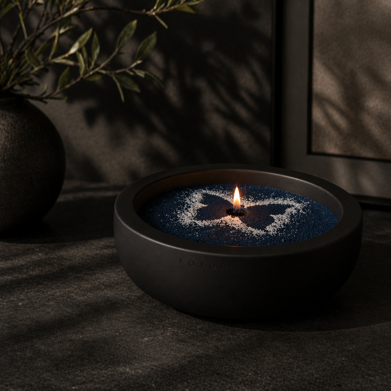 Black Luxe candle vessel filled with navy blue pearled wax, featuring a white butterfly design and a single lit flame, placed on a textured surface with moody lighting, soft shadows, and a decorative plant in the background.