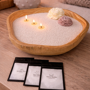 Lifestyle image featuring a handcrafted wood bowl candle filled with pearled wax, accented with decorative wax flowers and multiple lit wicks, accompanied by scent sample packets, styled in a warm, natural setting to highlight customization, fragrance variety, and a cozy, artisanal aesthetic.