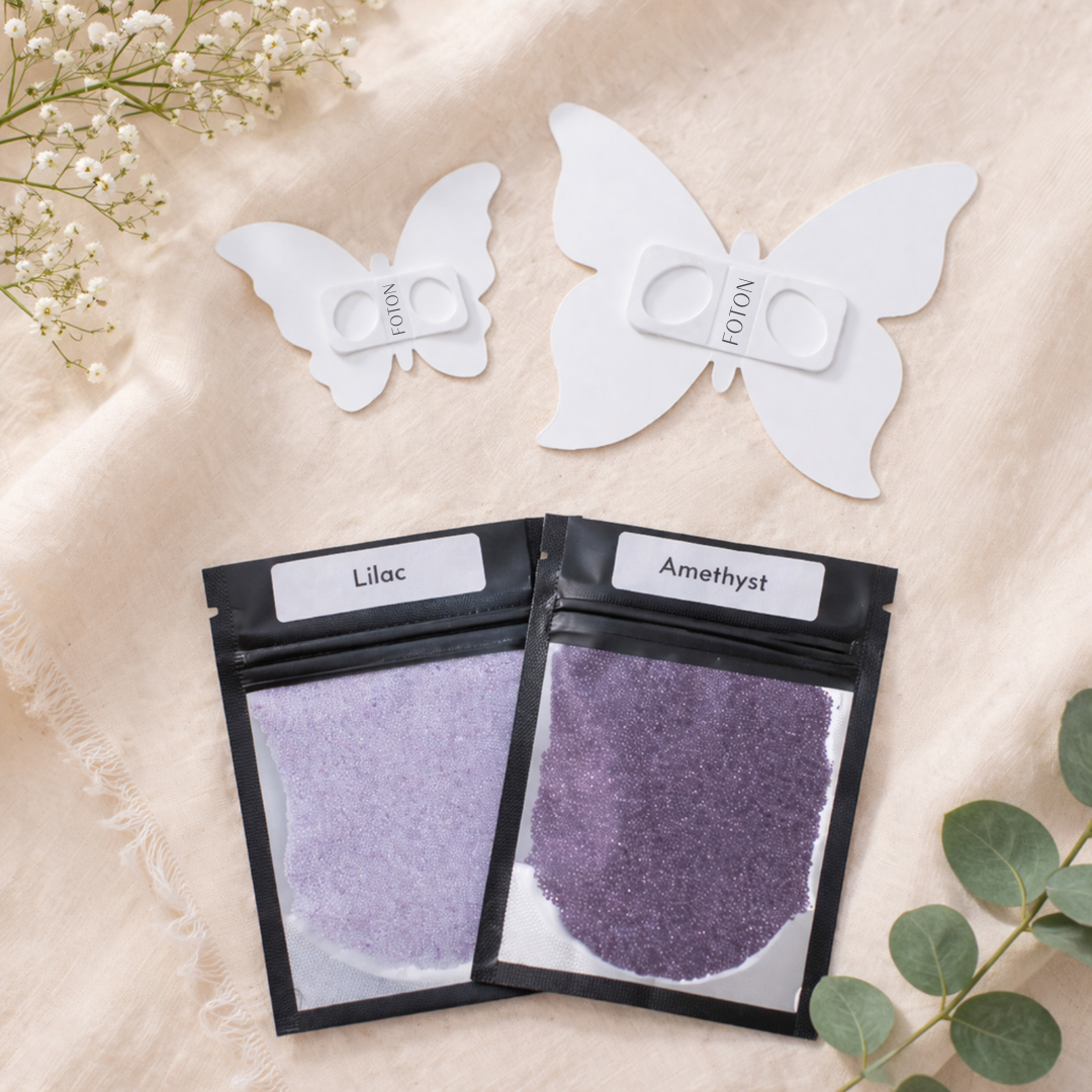 Two butterfly-shaped stencil tools alongside color sample pouches labeled Lilac and Amethyst, highlighting customization options for candle colors.