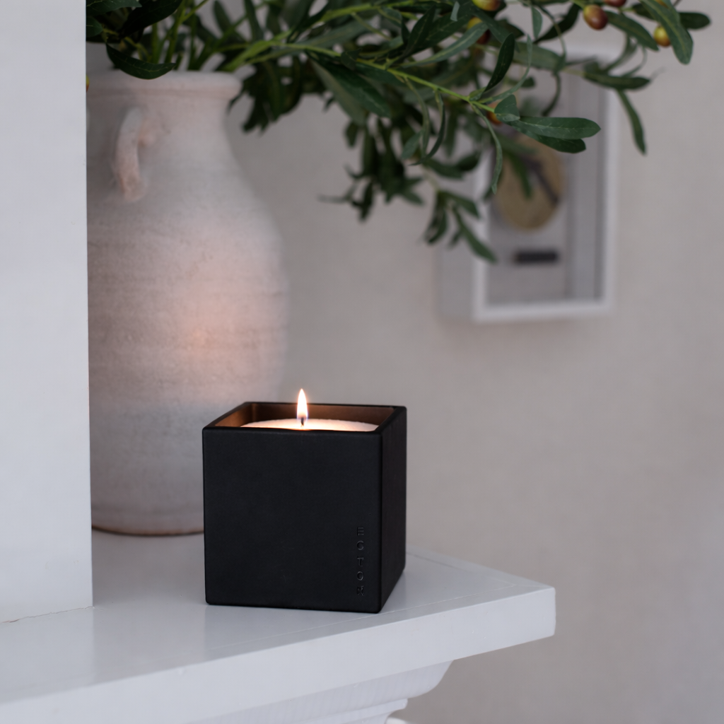 Lifestyle image of the Le Cube concrete candle in a deep black finish, styled on a clean shelf beside neutral décor and greenery, creating a calm, modern, and elevated home ambiance.