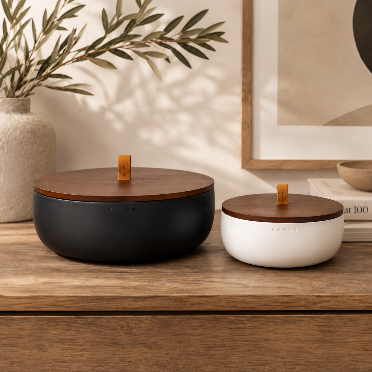 Matte black and white Luxe concrete candle bowls with matching wooden lids displayed on a warm wood console table in a modern home. The bowls are styled with neutral décor, ceramic vases, framed artwork, and soft natural light to highlight their timeless, minimalist design.
