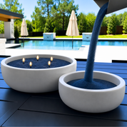 White Classic Luxe Concrete Bowl being refilled with navy Foton Candle pearls beside a swimming pool. The image demonstrates the easy refill process and the reusable design of the concrete candle vessel.