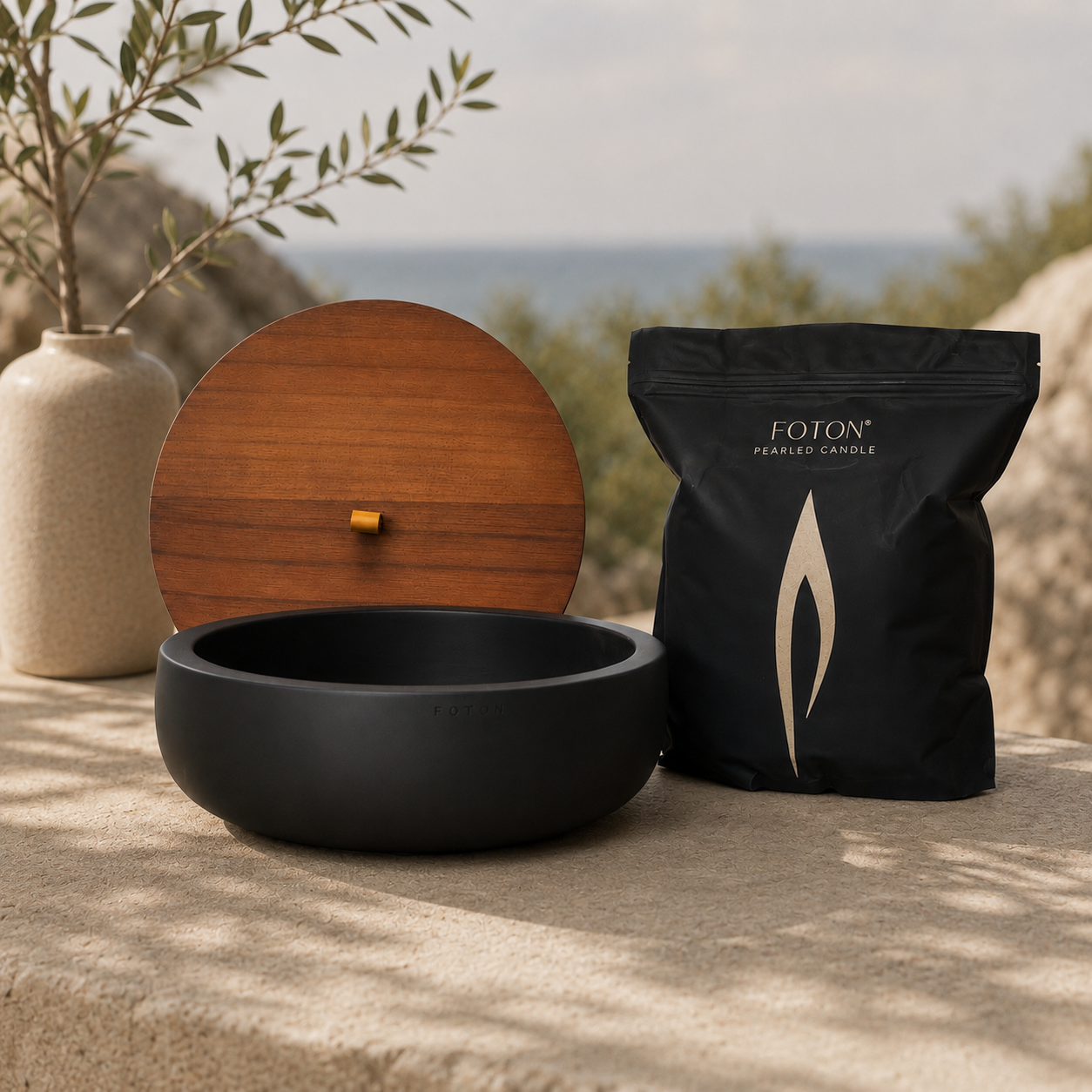 Matte black Oversized Luxe Concrete Bowl displayed with a matching wooden lid and Foton pearled candle refill bag in a natural outdoor setting. The image highlights the modern design and reusable candle system.