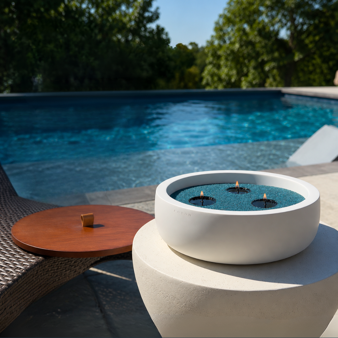 Oversized white Luxe Concrete Bowl filled with ocean blue candle pearls and three lit wicks beside its matching wooden lid. The image highlights the lid as a practical accessory for outdoor use.
