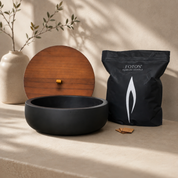 Matte black Oversized Luxe Concrete Bowl displayed with a matching wooden lid, Foton pearled candle refill bag, and XL wooden wicks in a warm, minimalist setting. The image showcases the complete oversized outdoor candle set.