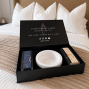 Open black Foton Pearled Candle luxury gift box displayed on a bed with white pillows, showing a white Luxe concrete bowl, two 18oz limited edition candles, and candle accessories inside. The inside lid reads “Turn almost anything into a candle” with social media icons and the handle @fotoncandle.