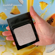 Product-focused image showcasing a Foton scent sample in “Malibu Mama – Fruity & Tropical,” featuring pearled wax in a compact packet held in hand, with vibrant tropical fruit visuals in the background to evoke a bright, refreshing, and beach-inspired fragrance experience.