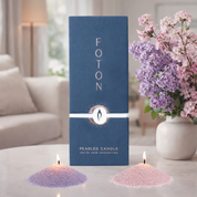 Foton candle packaging with two lit candles and a vase of flowers on a table.