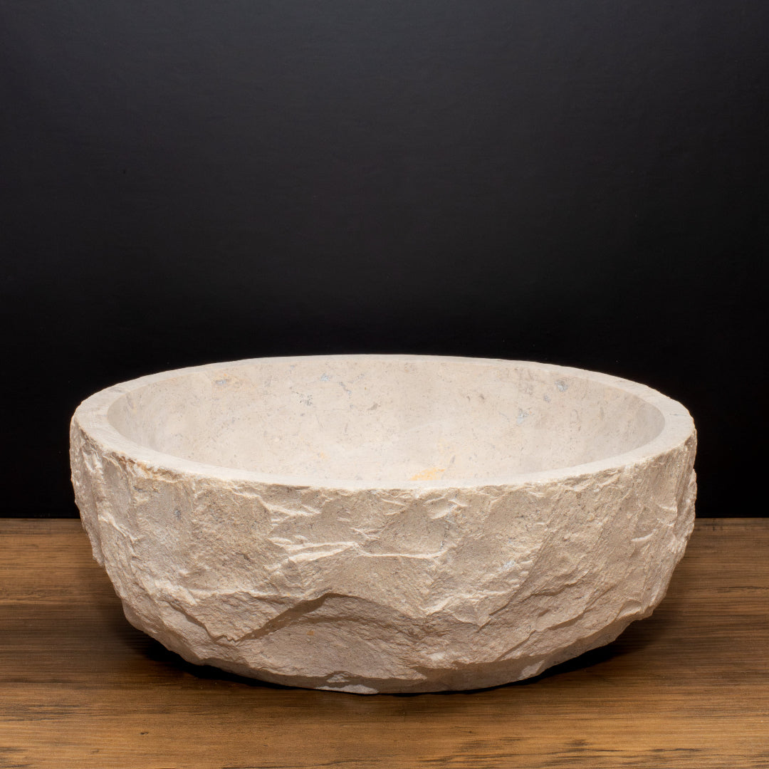 Product image featuring a large, textured limestone bowl with a raw, organic finish. Set against a dark backdrop on a wooden surface, the piece stands out for its natural, sculptural look, highlighting its potential as a statement vessel for candles or home décor.