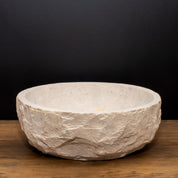 Product image featuring a large, textured limestone bowl with a raw, organic finish. Set against a dark backdrop on a wooden surface, the piece stands out for its natural, sculptural look, highlighting its potential as a statement vessel for candles or home décor.