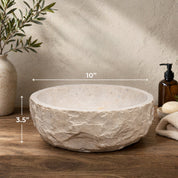 Decorative stone bowl with dimensions (10" x 3.5") on a wooden surface, next to a plant and bottles.