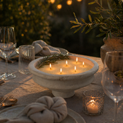 A warm, inviting lifestyle scene featuring a multi-wick Foton pearled candle set in an elegant stone vessel, glowing softly at the center of a beautifully styled outdoor table. Surrounded by glassware, linens, and natural greenery, the image captures a cozy, golden-hour ambiance that evokes relaxed gatherings and elevated everyday moments.