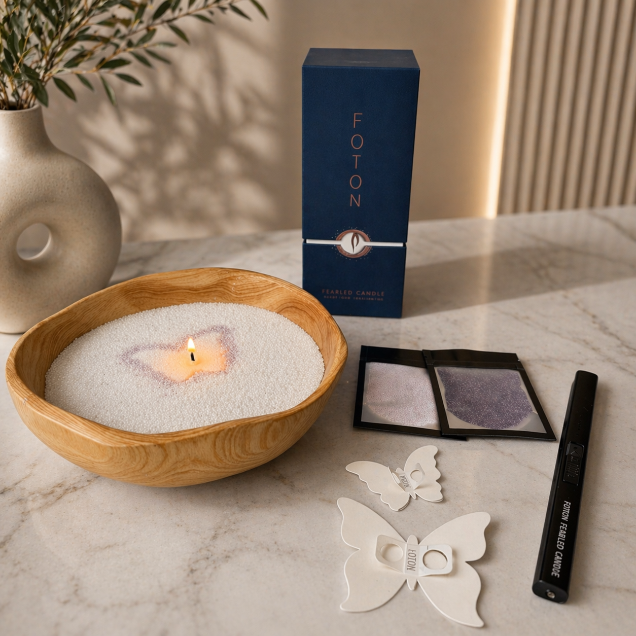 Foton candle set arranged on a marble surface, featuring a natural wood bowl filled with white pearled wax and a single lit wick with a subtle butterfly design. Next to it are a navy 18oz Foton box, two packets of colored wax samples in light and dark purple, two butterfly-shaped stencils, and a black electric lighter for candle use.