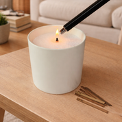 Lifestyle image of a Foton pearled candle in a minimalist white vessel, filled with white pearled wax and lit with a wooden wick. A sleek lighter is shown igniting the flame, with extra wooden wicks placed beside the candle, highlighting ease of use and a clean, modern home ambiance.