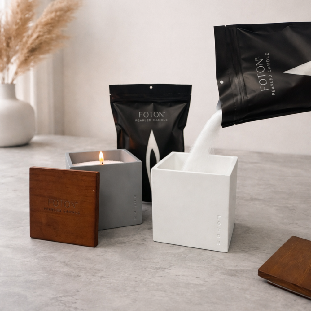 Product image showcasing the Foton pearled candle system, featuring refillable square vessels with wooden lids and premium pearled wax being poured from branded packaging, highlighting the clean, mess-free refill process, reusability, and modern, minimalist design.