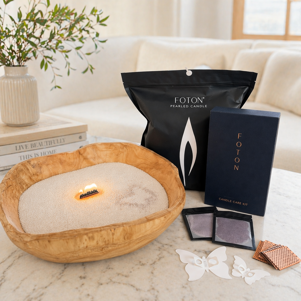 A styled lifestyle image showcasing a complete Foton candle setup, featuring a lit pearled candle in a handcrafted wooden bowl alongside a Grande bag, candle care kit, color samples, and decorative stencils. Set in a bright, cozy home environment, the composition highlights both the product’s versatility and its elevated, gift-ready presentation.